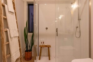 Een moderne badkamer met een glazen douchecabine, een houten trapje, een klein houten krukje en een kamerplant.