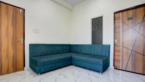 Une pièce avec un canapé d’angle turquoise, une porte en bois avec une plaque numérotée et un sol en marbre.