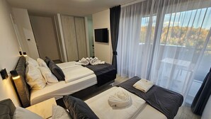 Ein Hotelzimmer mit zwei Betten, einem Fernseher, einem Kleiderschrank und einem Balkon mit Vorhängen.