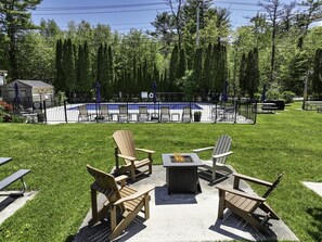 Un patio con sillas Adirondack, una chimenea y una piscina cercada.