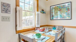 Un comedor con una mesa dispuesta para dos, una ventana con persianas, un letrero de bienvenida y un mapa en la pared.