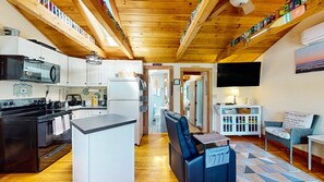 A modern kitchen with white cabinets, a black stove, and a wooden ceiling. - Coastal Shorelands Retreat + Walk-to-Beach Access and Pool (Kennebunk)