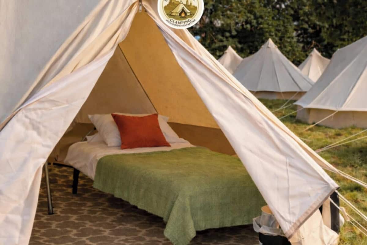A tent with a bed, a green blanket, and a red pillow.