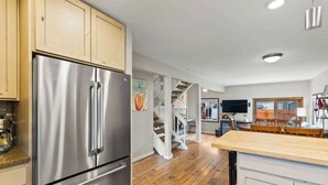 Una cocina con refrigerador de acero inoxidable, piso de madera y una escalera que lleva a otro nivel.