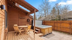 Una terraza de madera con un jacuzzi, asientos al aire libre y una pérgola.