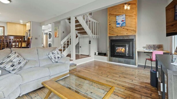 Un salón con sofá, mesa de centro, chimenea, piso de madera y una escalera.