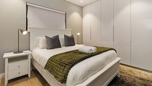 Ein Schlafzimmer mit einem Bett, Nachttischen, einem Kleiderschrank und einem Fenster mit Jalousien.