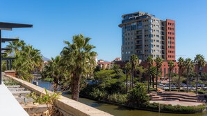 A riverside view with a modern building, palm trees, and a parking area. - Spacious Century City Apartment, Pool and Gym (Cape Town)