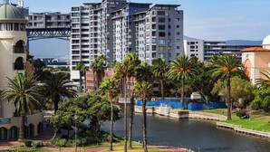 A waterfront hotel with a circular plaza, palm trees, and a bridge in the background. - Spacious Century City Apartment, Pool and Gym (Cape Town)