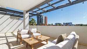 A rooftop terrace with a wooden table, two white sofas, and a pergola structure. - Spacious Century City Apartment, Pool and Gym (Cape Town)