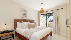 A modern bedroom with a bed, bedside table, lamp, and a city view through the window. - Spacious Century City Apartment, Pool and Gym (Cape Town)