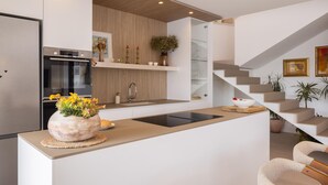 Cozinha moderna com ilha central, forno embutido e escada que leva a um andar superior.