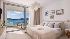 Quarto com cama, vista para o mar e varanda com cadeiras.