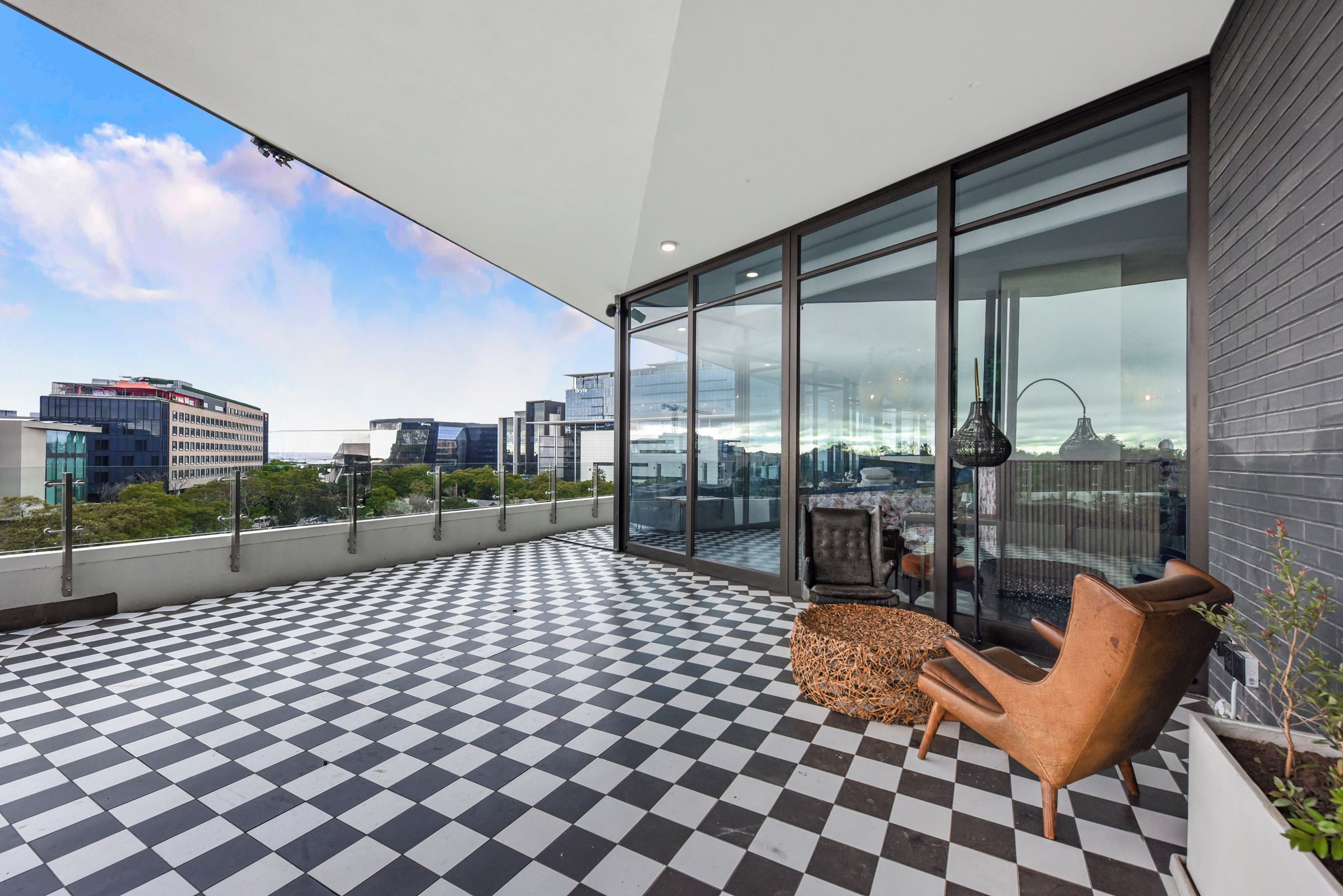Uma varanda moderna com piso xadrez, grandes portas de vidro e vista para a cidade.