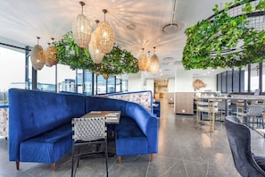 Un espace de détente moderne avec un canapé bleu, des lustres en cristal suspendus et une installation végétale verte.