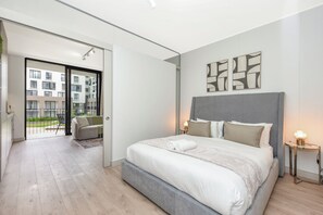 Ein modernes Schlafzimmer mit einem großen Bett, einem Balkon und Blick auf ein Wohngebäude.