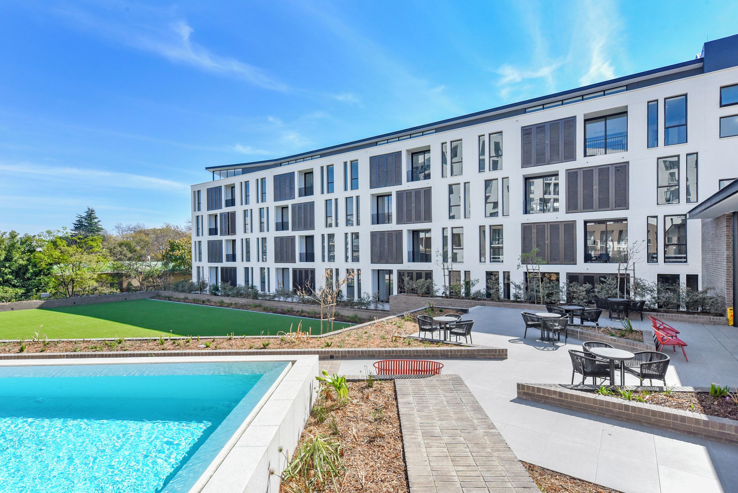 A modern building with a swimming pool, outdoor seating, and a well-maintained lawn.