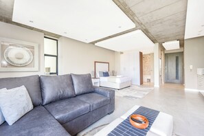 Ein modernes Wohnzimmer mit einem grauen Sofa, einem Couchtisch mit Fernbedienung und einem großen Wandventilator.
