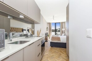 Ein modernes Hotelzimmer mit Küchenbereich, einem Bett mit Blick und einem Fischgrätparkett.
