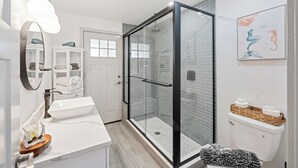 Uma casa de banho moderna com cabine de duche em vidro, lavatório branco e sanita com cestas de artigos de higiene pessoal.