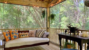 Una terraza de madera con una cama, almohadas, una mesa con velas y plantas colgantes.