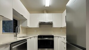Een moderne keuken met roestvrijstalen apparatuur, witte kastjes en een betegelde vloer.