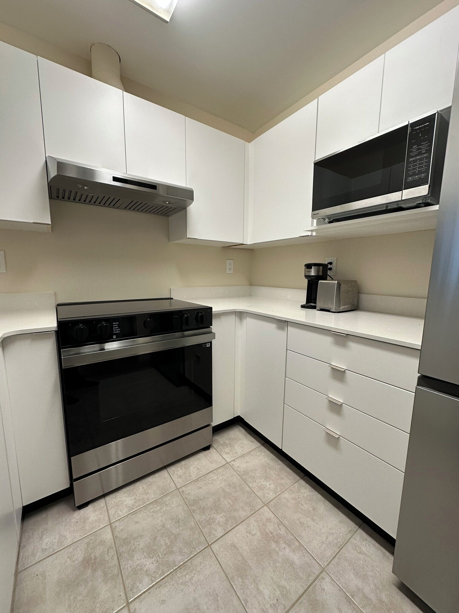 A kitchen with white cabinets, a stainless steel oven, a microwave, and a coffee maker.