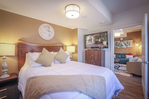 A hotel room with a large bed, a wooden headboard, a globe artwork, a television, and a door leading to another room.
