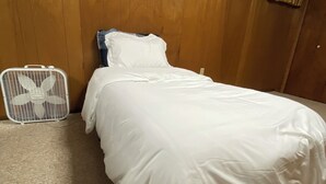 Een bed met witte beddengoed in een kamer met houten wanden en een plafondventilator.