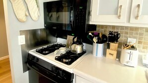 Een keuken met witte kastjes, een zwarte kookplaat en een magnetron.
