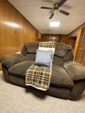 A gray sofa with a plaid blanket and a striped pillow, a ceiling fan, and wooden walls. - Under The Cherry Boon: A Traverse City Dream (Traverse City)