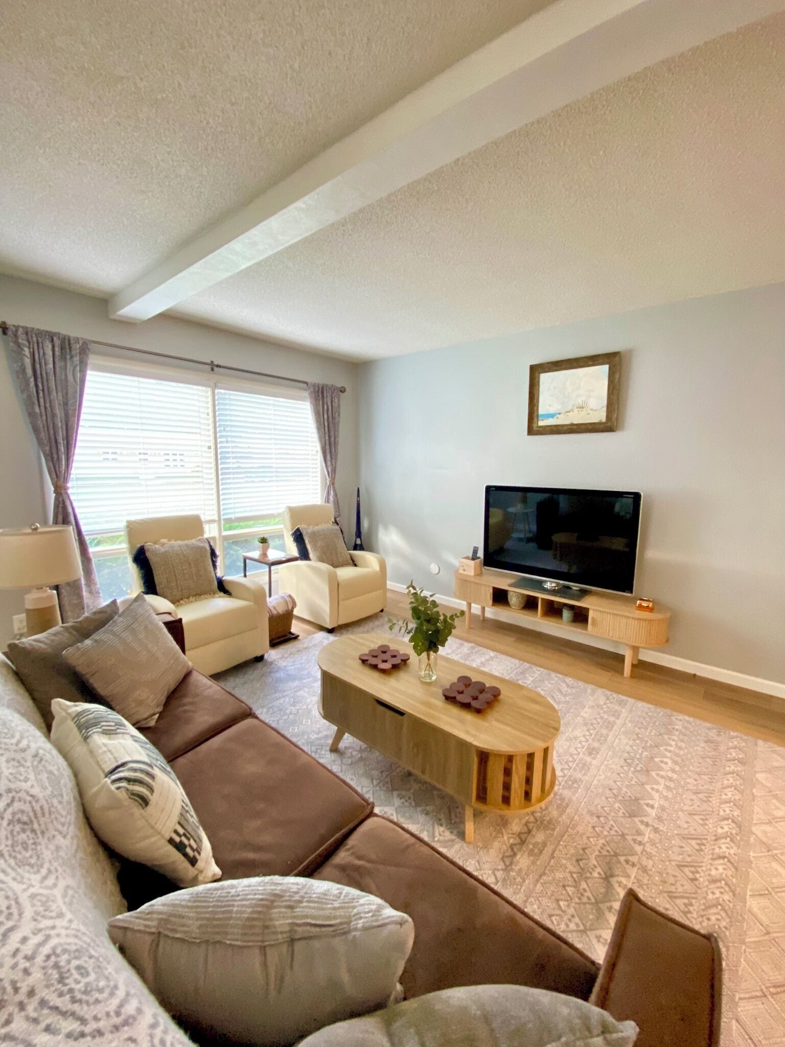 Ein Wohnzimmer mit einer Couch, Sesseln, einem Couchtisch, einem Fernseher und einem Fenster mit Vorhängen.
