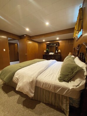 A hotel room with a large bed, wooden paneling, a mirror, and a nightstand. - Under The Cherry Boon: A Traverse City Dream (Traverse City)