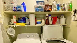 Een wasserette met twee voorladers, bovenliggende planken met schoonmaakmiddelen en een toiletpapierhouder aan de muur.