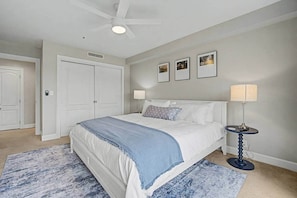 A bedroom with a bed, a ceiling fan, a nightstand with a lamp, and a door.