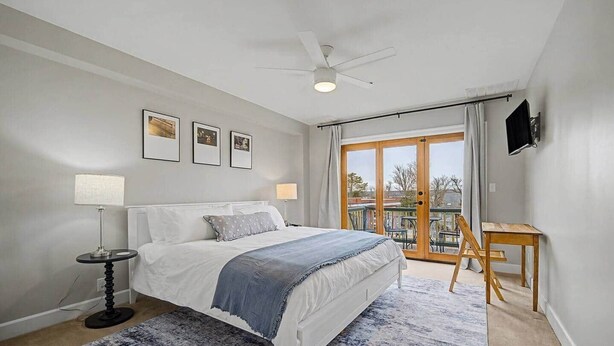 Une chambre avec un lit, un bureau, une chaise, un ventilateur de plafond et un balcon avec vue.