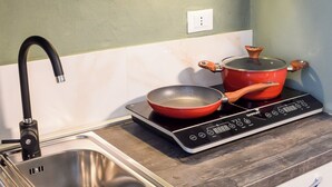Une cuisine dotée d’un évier en acier inoxydable, d’un robinet noir, d’une casserole rouge posée sur une plaque de cuisson à induction et de meubles blancs.