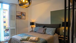 Une chambre à coucher avec un lit, des lampes de chevet, un luminaire au plafond, un tableau au mur et une vue à travers une porte coulissante.