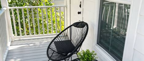 A porch with two black chairs, a small table, and a potted plant.