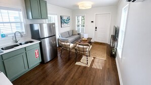 A compact kitchen with a built-in refrigerator, a dining area with wicker chairs, and a living space with a sofa. - The Pass Picture Book (Pass Christian)