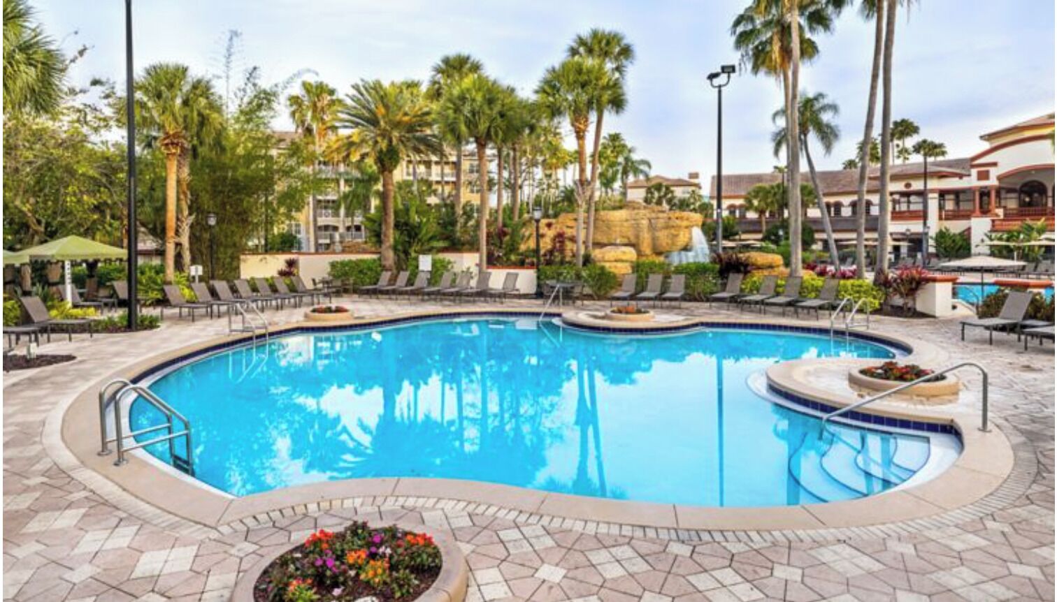 A swimming pool with lounge chairs, palm trees, and a waterfall feature.