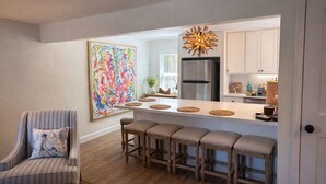 A modern kitchen with a stainless steel refrigerator, a bar area with stools, and a large abstract painting on the wall. - A Porter Retreat • 2BR Walk to Downtown OS (Ocean Springs)
