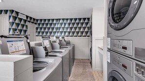 A laundry facility with multiple washing machines and dryers, a patterned wall, and a floor mat. - A Porter Retreat • 2BR Walk to Downtown OS (Ocean Springs)