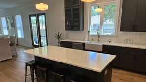 Una cocina con una isla grande, taburetes de bar, armarios oscuros e iluminación colgante.