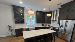 Una cocina moderna con una isla central, muebles oscuros, electrodomésticos de acero inoxidable e iluminación colgante.