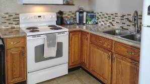 Una cocina con armarios de madera, estufa blanca, microondas y salpicadero de azulejos.