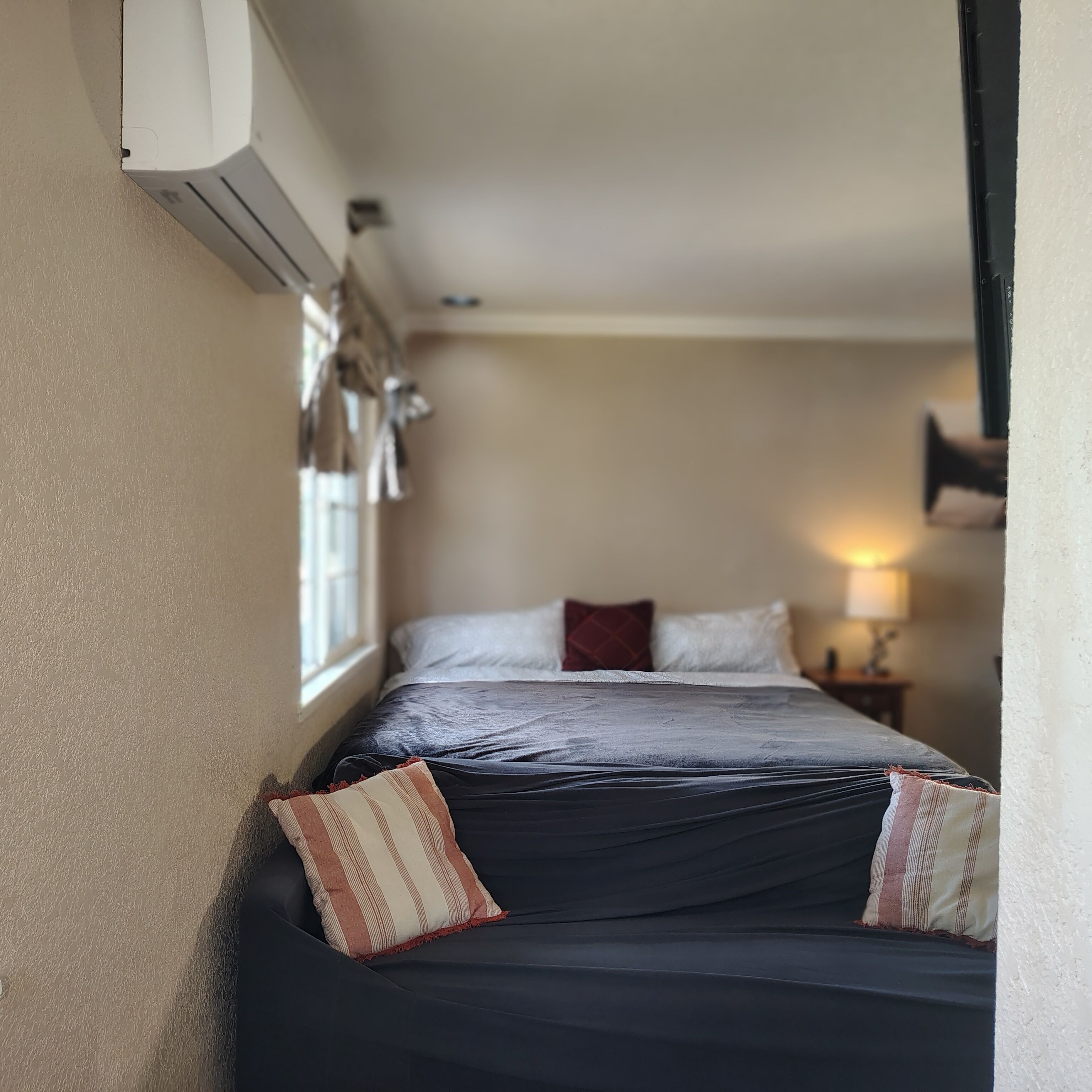 A narrow room with a bed, a window, and a wall-mounted air conditioner.