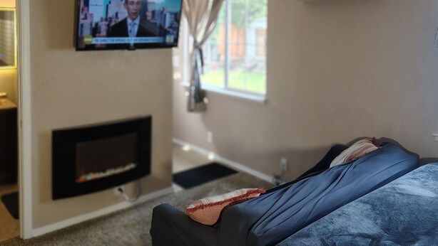 Una sala de estar con televisión, chimenea, ventilador de techo y ventana.