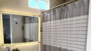 Un baño con lavamanos, espejo, planta en maceta y cortina de ducha a rayas.