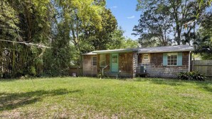 A small wooden house with a green door and windows, surrounded by trees and a grassy yard. - The Downtown Cedar - walk to Government St & Washington (Ocean Springs)